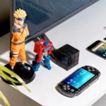 Flatlay photo of Naruto figure, Transformer figure, and several devices including an Android phone, PSP, and flatscreen.